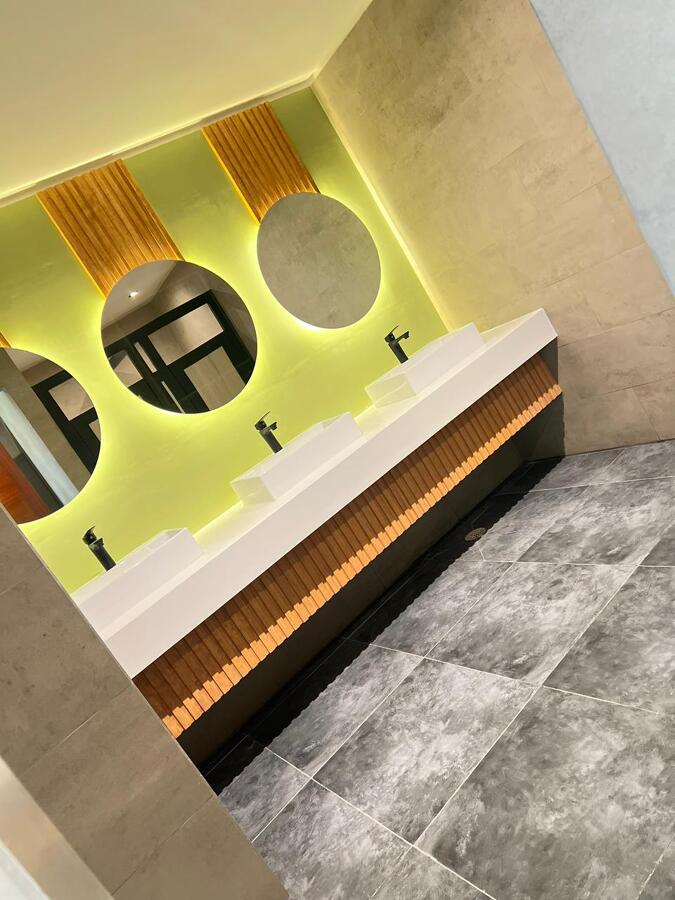 Baño moderno con mesón triple, espejos LED y revestimientos de madera.