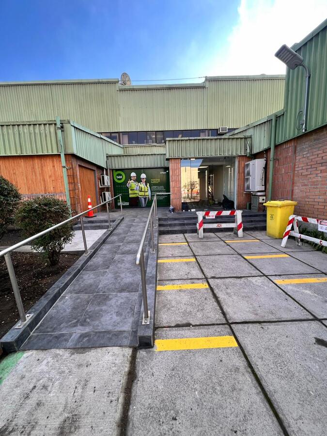 Acceso exterior con rampa, revestimiento de piso y pasamanos inoxidable.