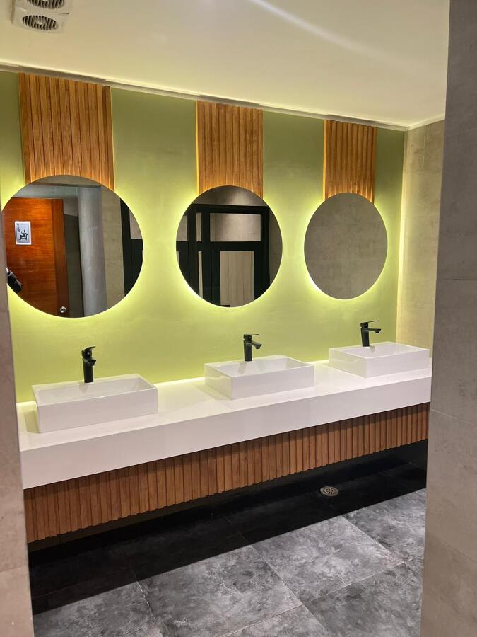 Baño terminado — mesón, espejos retroiluminados y revestimiento en madera