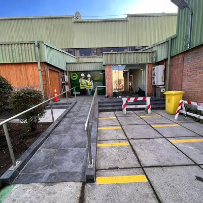 Acceso exterior con rampa, revestimiento de piso y pasamanos inoxidable.
